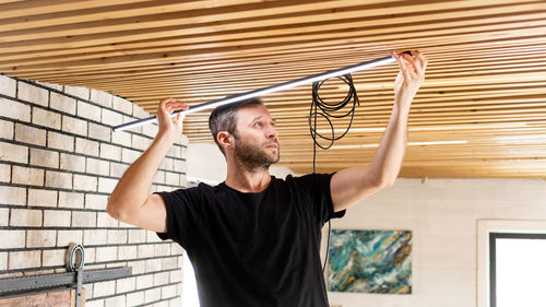 An electrician installs low voltage led lamps in a pine plank ceiling.  lamps raplacement service.