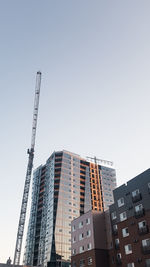 Low angle view of crane by building against clear sky
