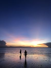 Silhouette people on beach against sky during sunset