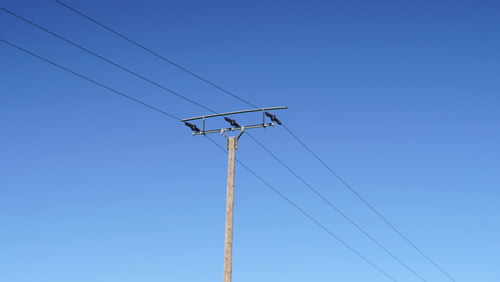 Low angle view of electricity pylon against clear blue sky