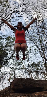 Low angle view of young woman in mid-air against bare tree
