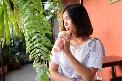 Young woman drinking juice while looking away at sidewalk cafe