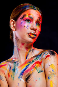 Shirtless young woman with colorful paints on her body against black background