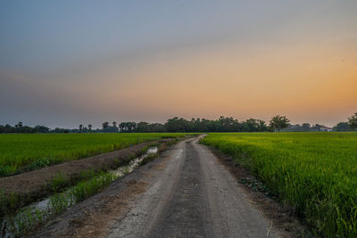 Road amidst field against sky during sunset