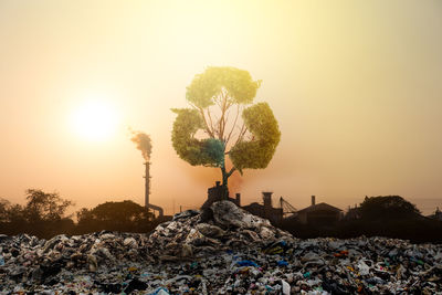 Digital composite image of recycling symbol over garbage and factory against orange sky