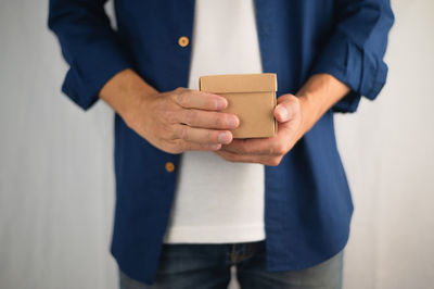 Midsection of man holding camera while standing against wall