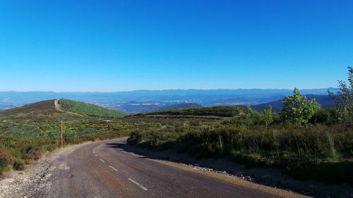 Empty road leading towards mountains against blue sky