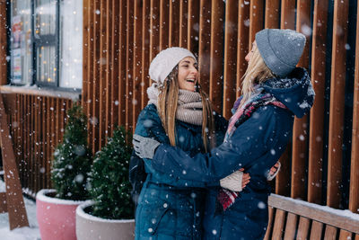 Adult female friends embracing and laughing rejoicing at the snowy cold weather.