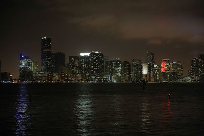 Illuminated cityscape by river against sky at night