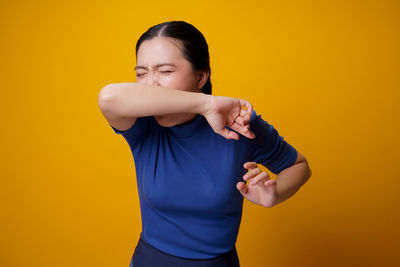 Young woman standing against yellow background