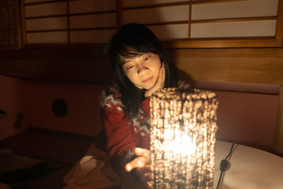 Thoughtful woman touching illuminated lamp at home