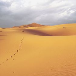 Scenic view of sand dunes against cloudy sky