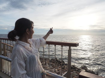 Rear view of woman standing by railing against sea