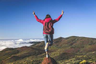 Rear view of woman with backpack gesturing peace sign while looking at landscape