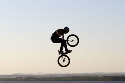 Man with bicycle jumping over sea against clear sky