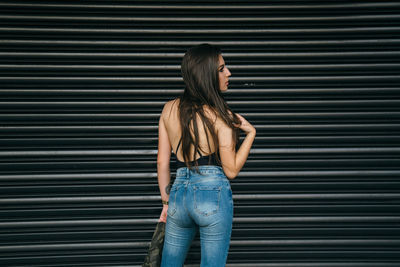 Young woman looking away while standing against wall