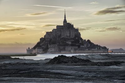 Built structure by sea against sky during sunset