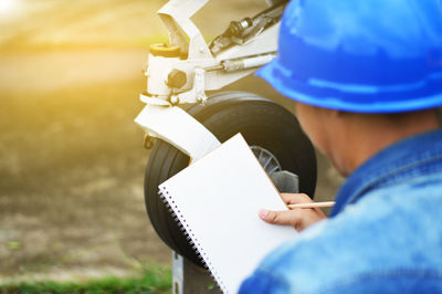 Close-up rear view of manual worker holding book while working at airport runway