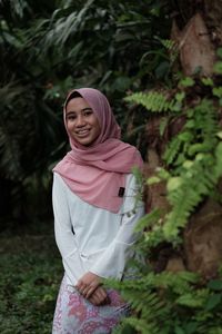 Portrait of smiling teenage girl wearing hijab standing by plants at park