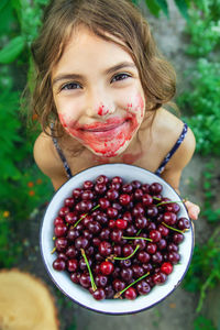 Portrait of happy girl with messy face holding bowl of cherries