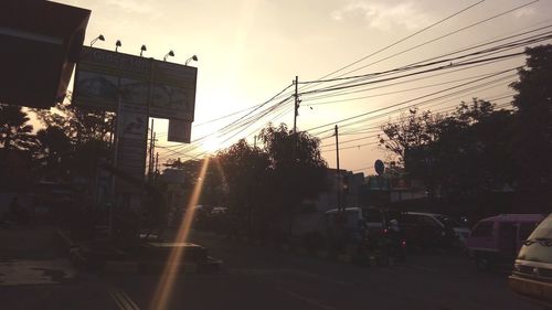 Cars on city street against sky during sunset