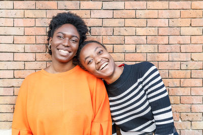 Cheerful african american female friends standing near building with brick wall on street