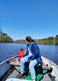 Teenage girl sitting on boat in river against clear sky