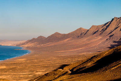 Scenic view of sea and mountains against clear blue sky