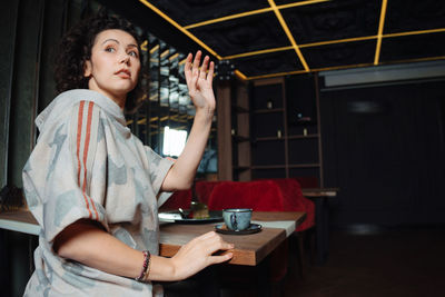 Portrait of young woman looking away while sitting on table