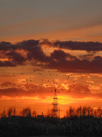 Silhouette electricity pylon on field against romantic sky at sunset