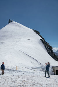 People standing on snowcapped mountain against clear sky