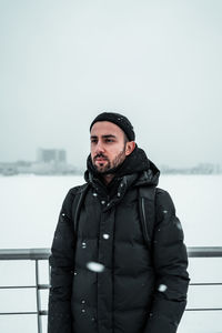 Young man standing by railing against sky during winter