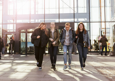 Full length of happy friends walking against railroad station in city