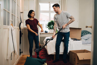 Woman gesturing while man holding golf club by bed in bedroom during relocation