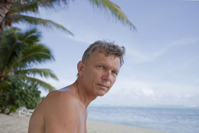 Portrait of shirtless man by sea against sky