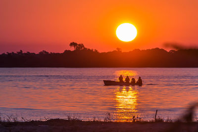 Silhouette boat in sea against orange sky