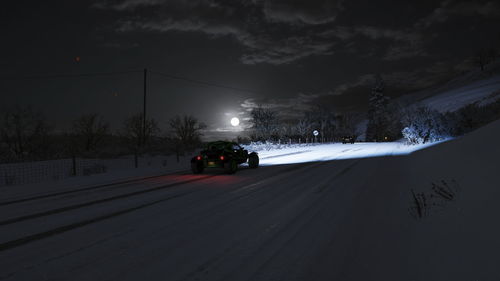 Car on snow covered road against sky at night
