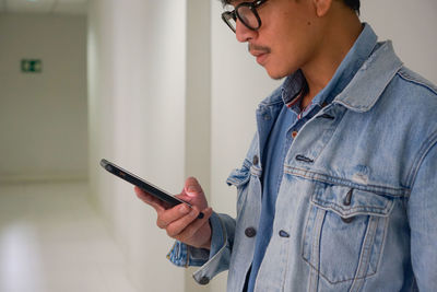 Midsection of man using mobile phone while standing against wall