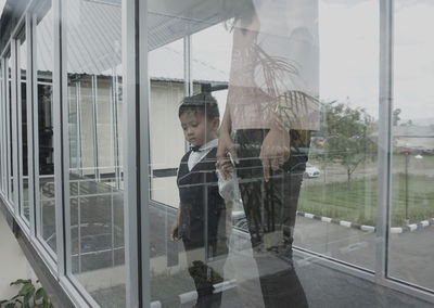 Midsection of mother with son looking through glass window