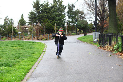 Portrait of boy riding push scooter on street against trees