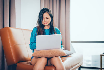 Young woman using phone while sitting on chair