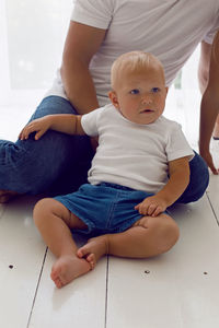 Father with son sitting on a white wooden floor in a large room