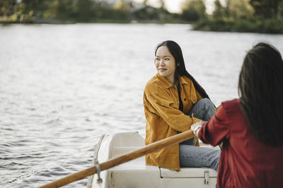 Woman looking away while female friend rowing boat on lake