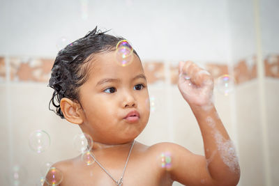 Close-up of shirtless girl playing with bubbles in bathroom