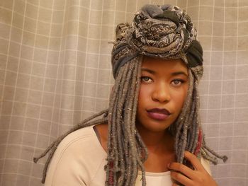 Portrait of young woman in headwear against curtain