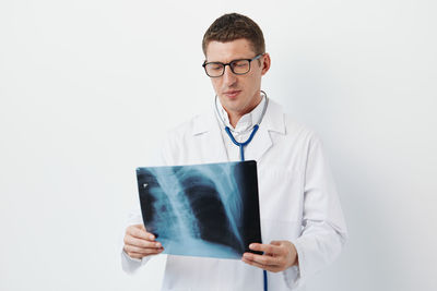 Portrait of doctor holding stethoscope against white background