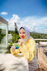 Portrait of young woman standing against sky