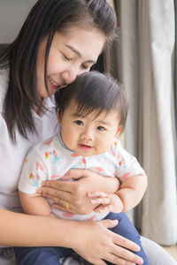 Close-up of mother holding baby sitting at home