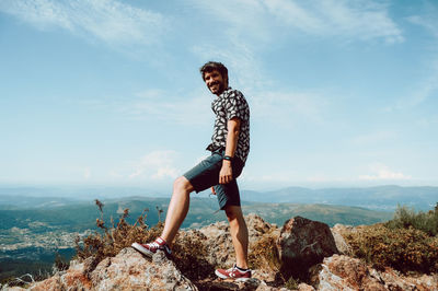 Young man standing on rock against sky