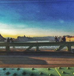 People walking on bridge in city at sunset